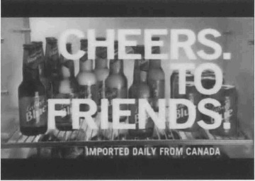 Exhibit G:  Bottles and cans of beer on the shelf in a refrigerator with the caption 'Cheers. To Friends. Imported Daily  From Canada'.