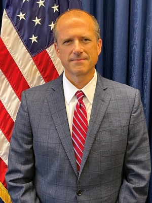 David M. Toepher standing in front of US flag and blue background