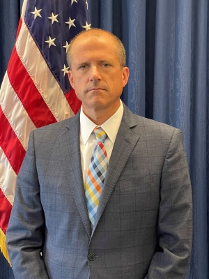 David M. Toepher standing in front of US flag and blue background
