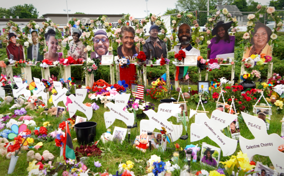 Cutouts of victims stand dove signs that show their respective names with the word "peace". Numeous flowers and bouquets fill the space.