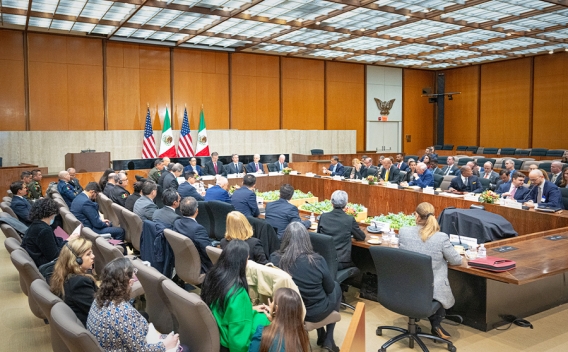 US and Mexico Officials and staff sit around a large table for discussion. The flags of the United States flag and Mexico are seen where the officials sit