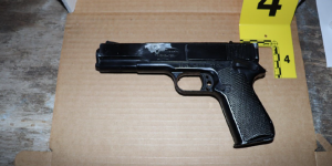 FBI evidence photo: black BB gun that looks similar to a semiautomatic hand gun, laying on a cardboard box with a crime scene marker labeled number 4 next to it.
