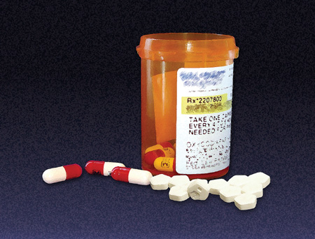 Photo of red and white capsules and pentagon-shaped white pills next to a prescription bottle containing some red and white capsules.