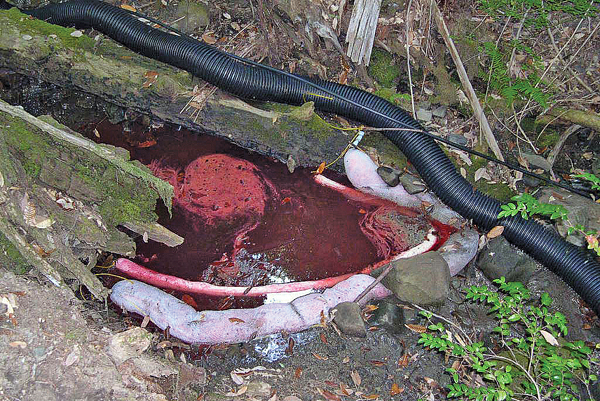 Photo showing barriers being used to contain a red diesel fuel spill from an outdoor generator into a natural waterway.