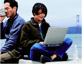 Photo of man looking thru a camera and woman working on a laptop sitting across the Bay Bridge in San Franciso