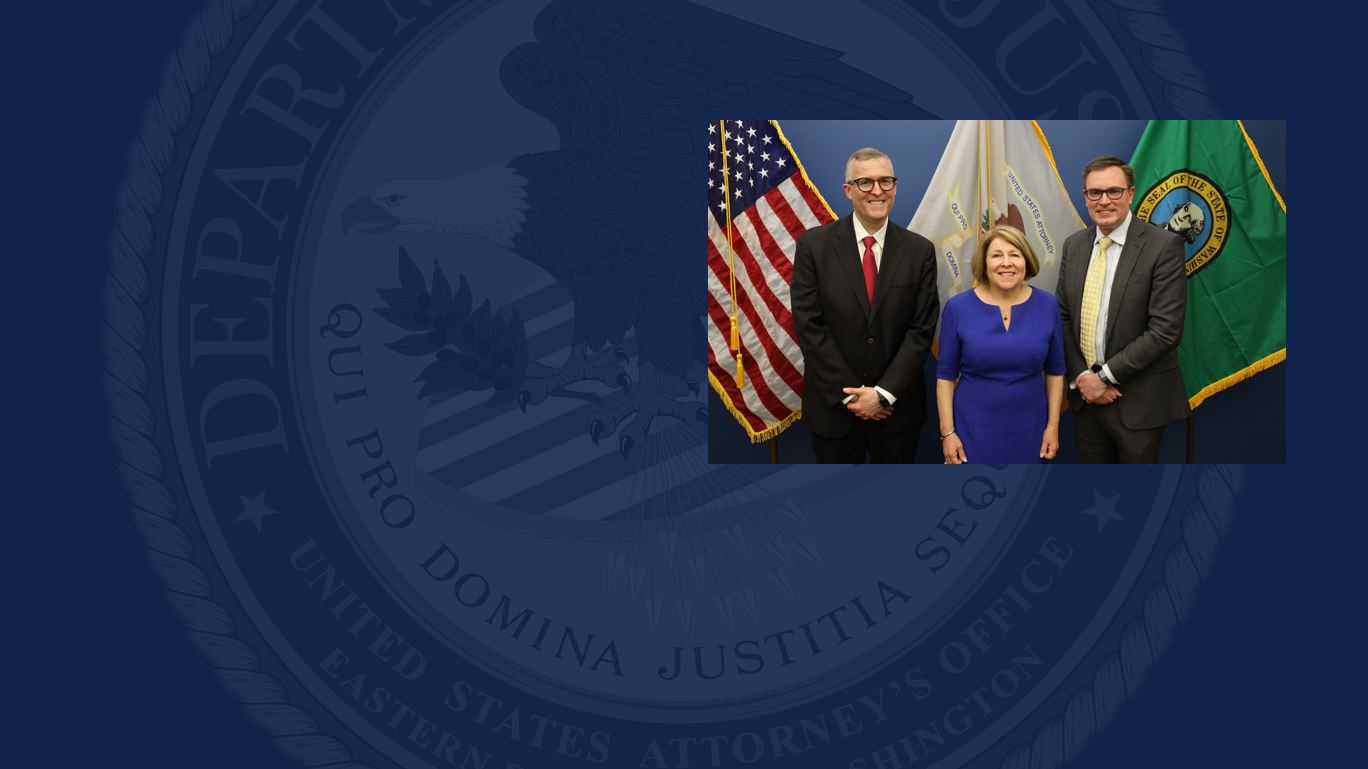 Three people pose for a photo in front of three flags 