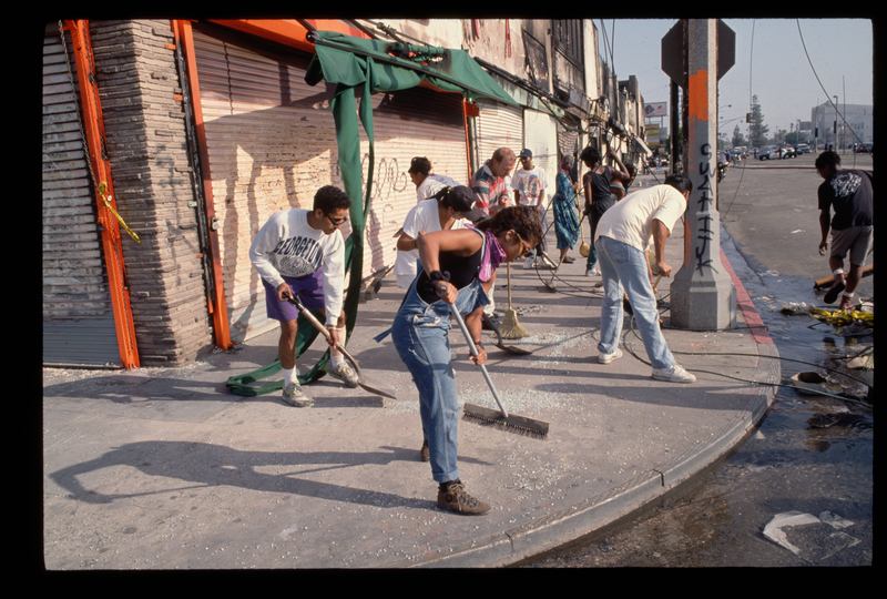 Community members clean up city streets with brooms and shovels following riots in Los Angeles. 