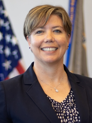 US Attorney Rebecca C Lutzko standing in front of flags