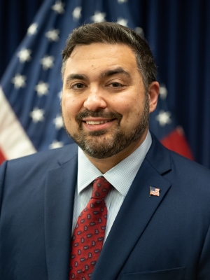 Headshot of US Attorney Nicholas Ganjei in front of American flag