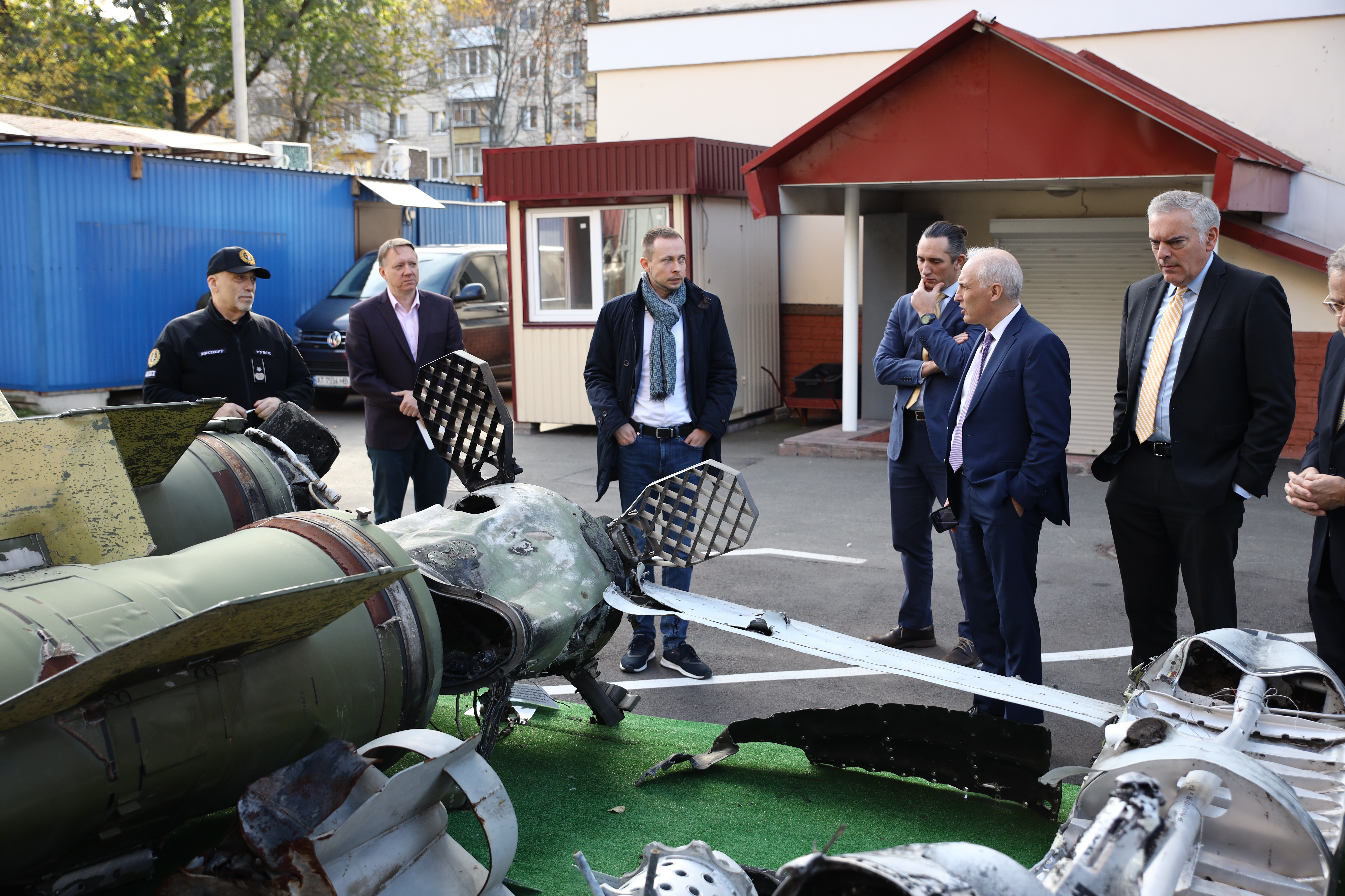 Six men stand in an outdoor lot in front of various pieces of mechanical equipment.
