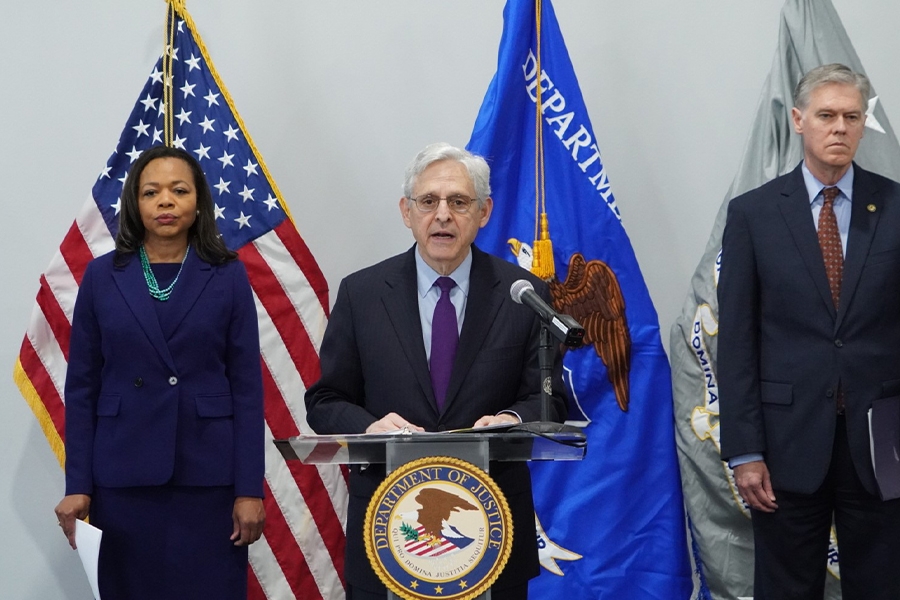 Attorney General Merrick B. Garland delivers remarks from a podium at the U.S. Attorney's Office for the Middle District of Florida. To the left is Assistant Attorney General for Civil Rights Kristen Clark. To the right is United States Attorney for the Middle District of Florida Roger B. Handberg