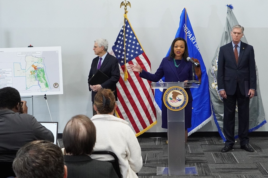 Assistant Attorney General for Civil Rights Kristen Clarke points out areas where redlining has occurred in Florida while delivering remarks from a podium at the U.S. Attorney's Office for the Middle District of Florida. To the left is Attorney General Merrick B. Garland. To the right is United States Attorney for the Middle District of Florida Roger B. Handberg