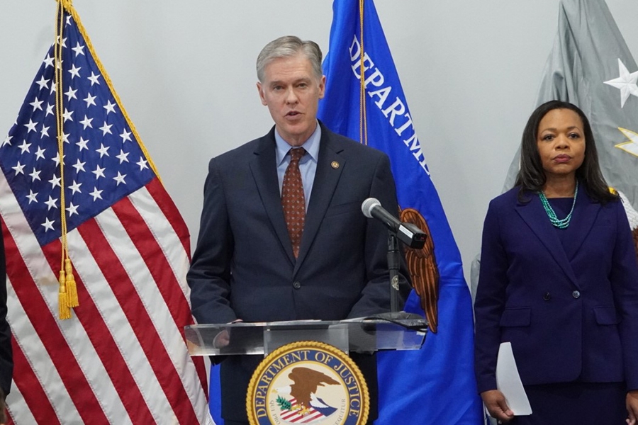 U.S. Attorney Roger B. Handberg delivers remarks from a podium at the U.S. Attorney's Office for the Middle District of Florida. To the right is Assistant Attorney General for Civil Rights Kristen Clarke