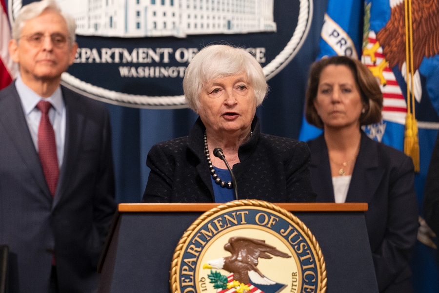 Secretary of the Treasury Janet L. Yellen delivers remarks from a podium at the Department of Justice. To the left is Attorney General Merrick B. Garland, and to the right is Deputy Attorney General Lisa O. Monaco.