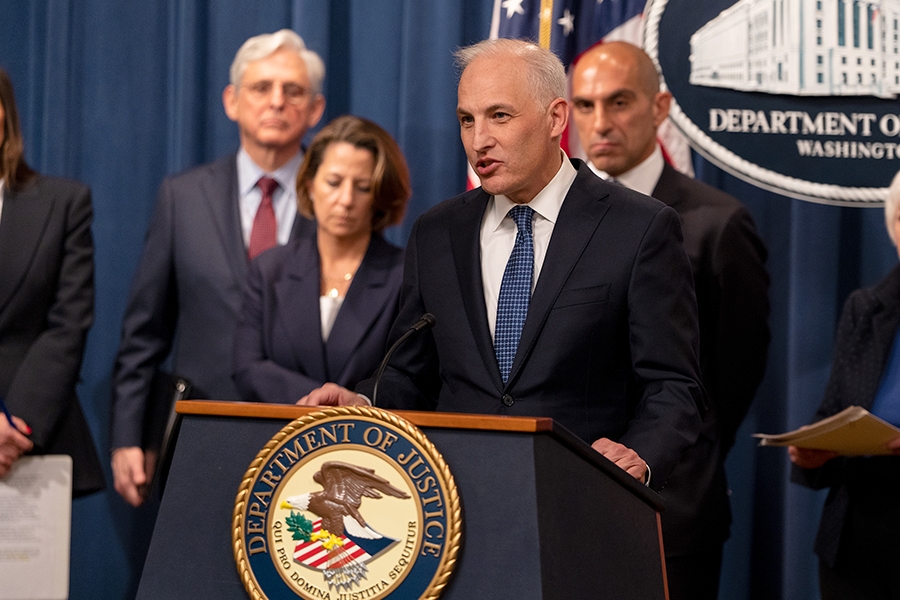 Assistant Attorney General for National Security Matthew G. Olsen delivers remarks from a podium at the Department of Justice. To the left is Attorney General Merrick B. Garland and Deputy Attorney General Lisa O. Monaco; behind him is Chairman Rostin Behnam of the Commodity Futures Trading Commission (CFTC).