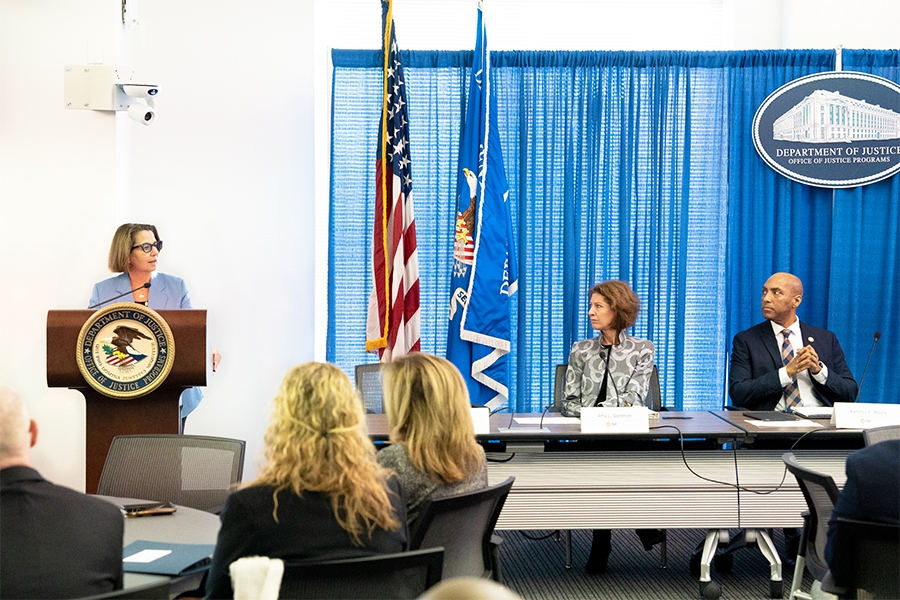 Deputy Attorney General Lisa O. Monaco delivers remarks from a podium at the Office of Justice Programs. She is joined by Assistant Attorney General for the Office of Justice Programs Amy Solomon and Director of the Bureau of Justice Assistance Karhlton F. Moore.