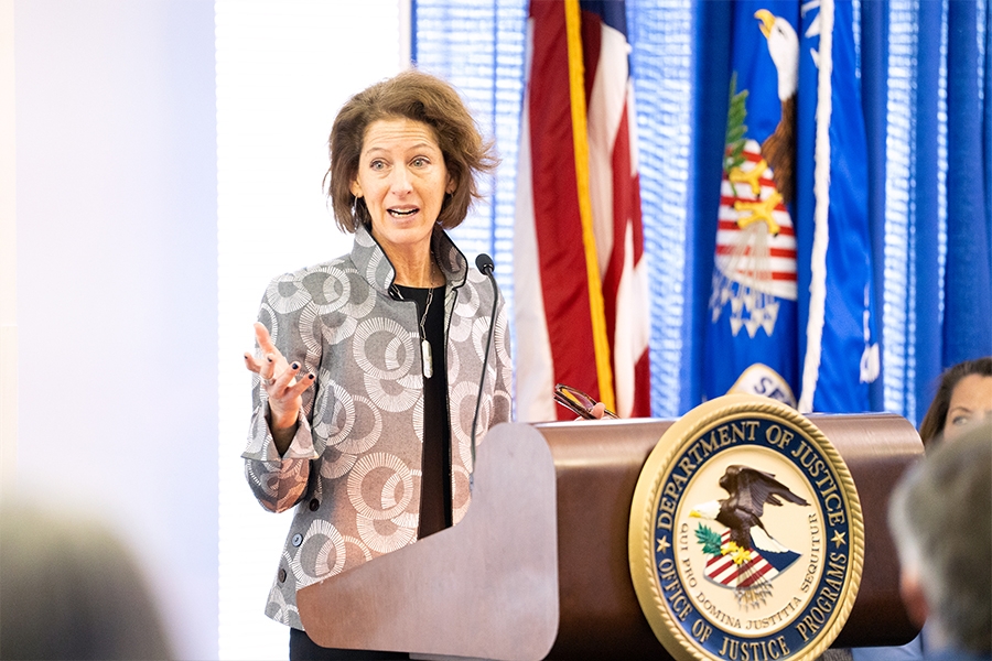 Assistant Attorney General for the Office of Justice Programs Amy Solomon delivers remarks from a podium at the Office of Justice Programs. Assistant Attorney General for the Office of Justice Programs Amy Solomon delivers remarks from a podium at the Office of Justice Programs.