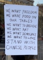 White sign with black writing which reads:WE WANT FREEDOM WE WANT FOOD ON OUR TABLES WE WANT TO BREATHE WE WANT ART WE WANT DEMOCRACY WE WANT TO LOVE STAND WITH CHINESE PEOPLE