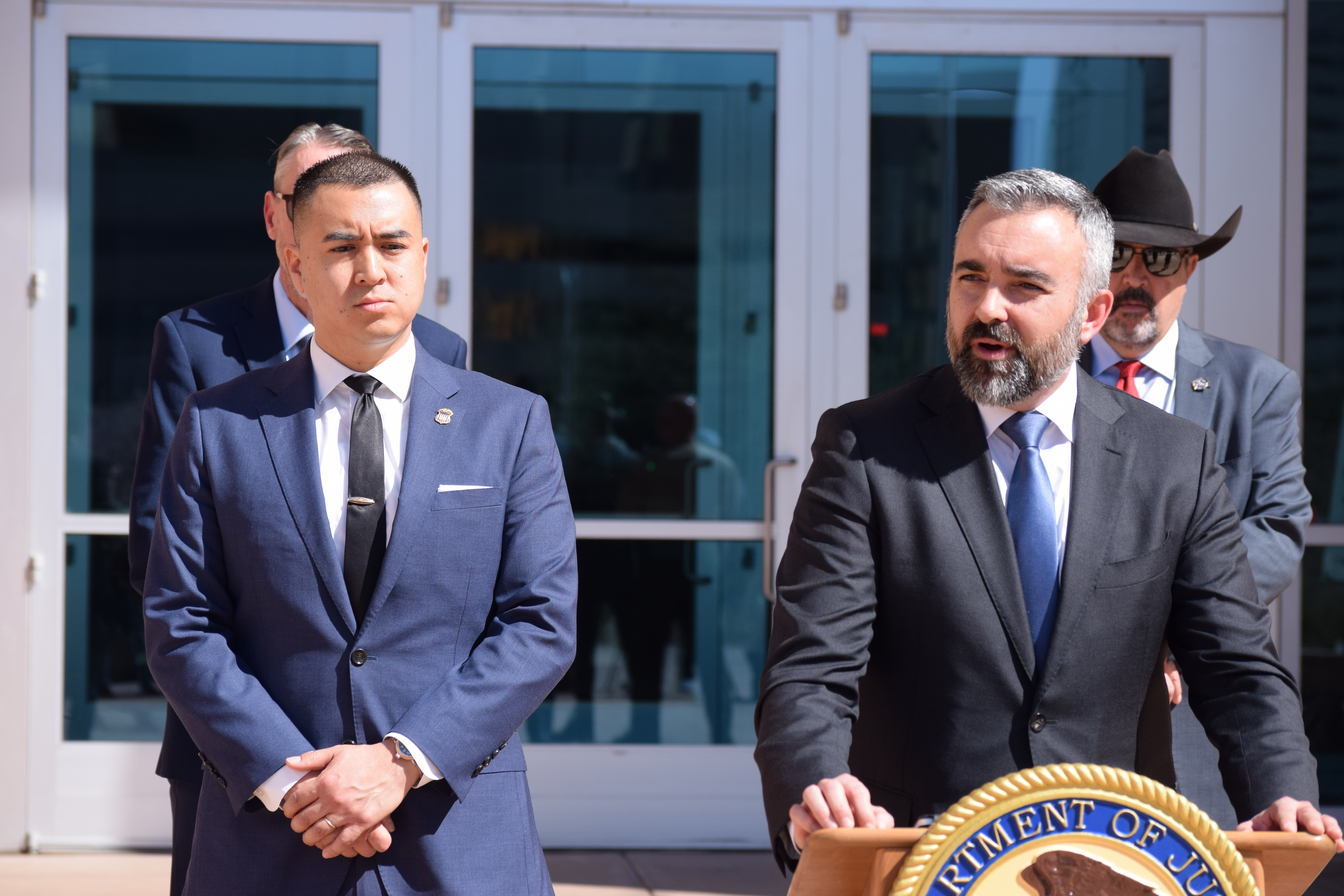 A man talking at a podium while two men watch from behind him