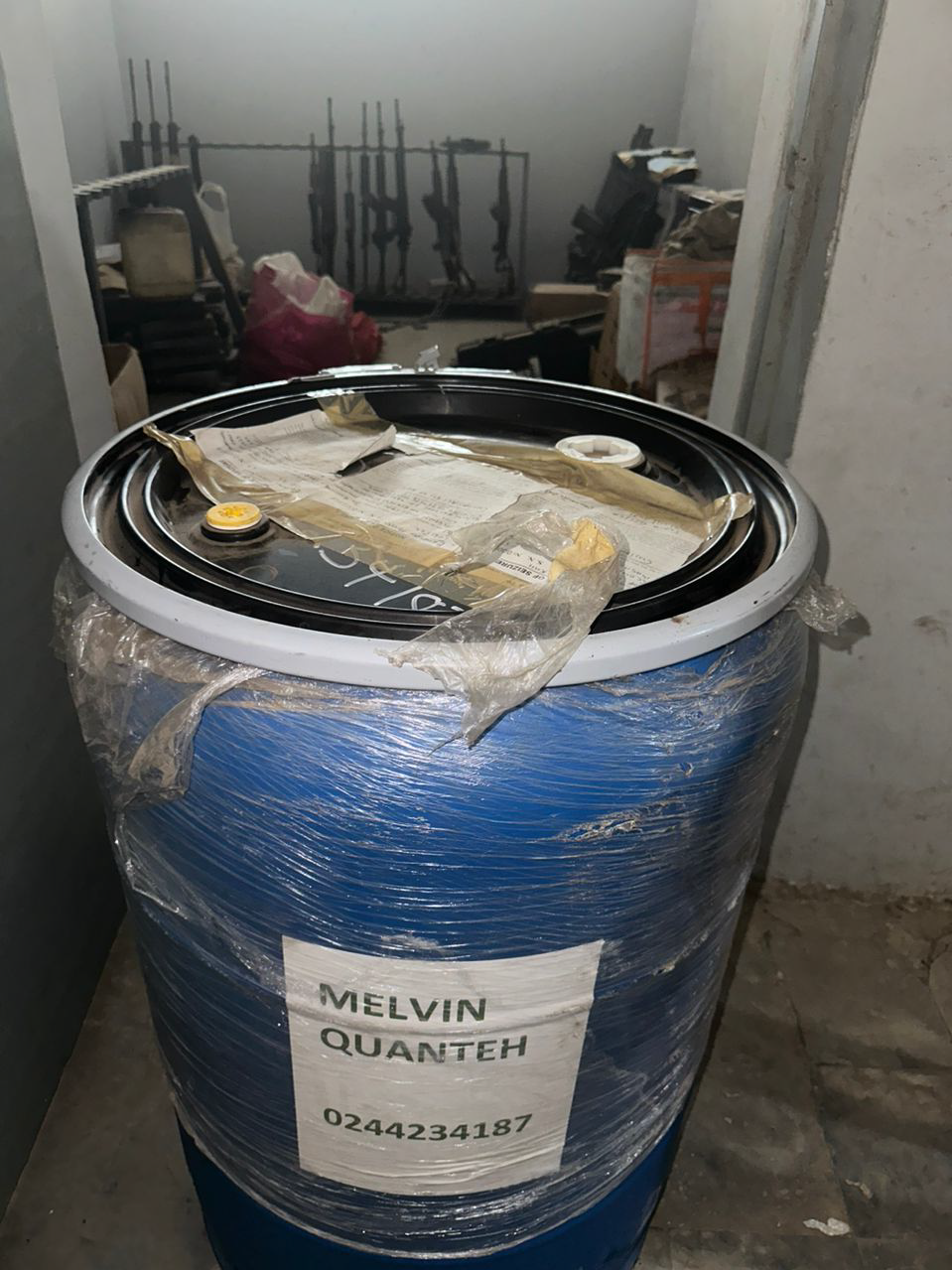 Blue barrel with text and firearms in the background