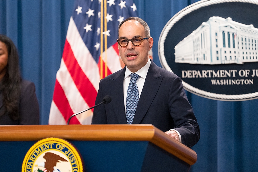 Assistant Attorney General Jonathan Kanter of the Justice Department’s Antitrust Division delivers remarks from a podium at the Department of Justice. He is joined by Department of Justice and federal government officials.