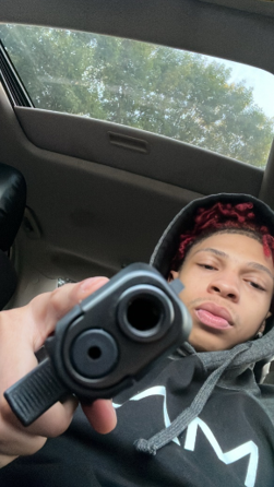A selfie showing a man pointing a gun at the camera.