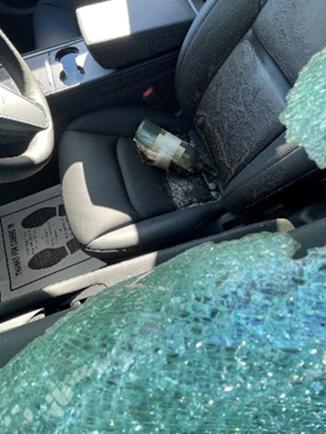 A broken bottle atop a black car seat with shattered car window visible. 