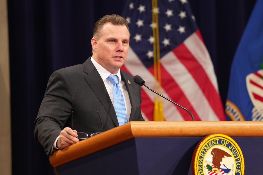 Deputy Assistant Attorney General Michael E. Gates delivers remarks at a podium in the Great Hall at the Department of Justice.