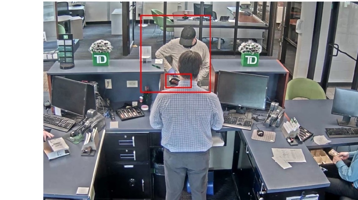 Man lifting his shirt and showing a bank teller a wooden handle at his waist