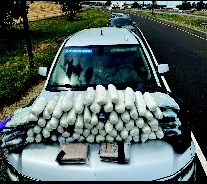 Seized drugs displayed on hood of law enforcement vehicle. 