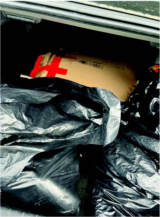 Black trash bags and box holding illicit drugs in trunk of vehicle. 