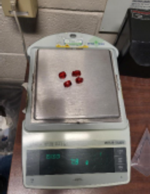 Four small red gummies on a stainless steel digital scale.