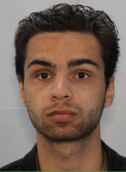 Photo of a man with dark hair and a dark shirt against a white wall.