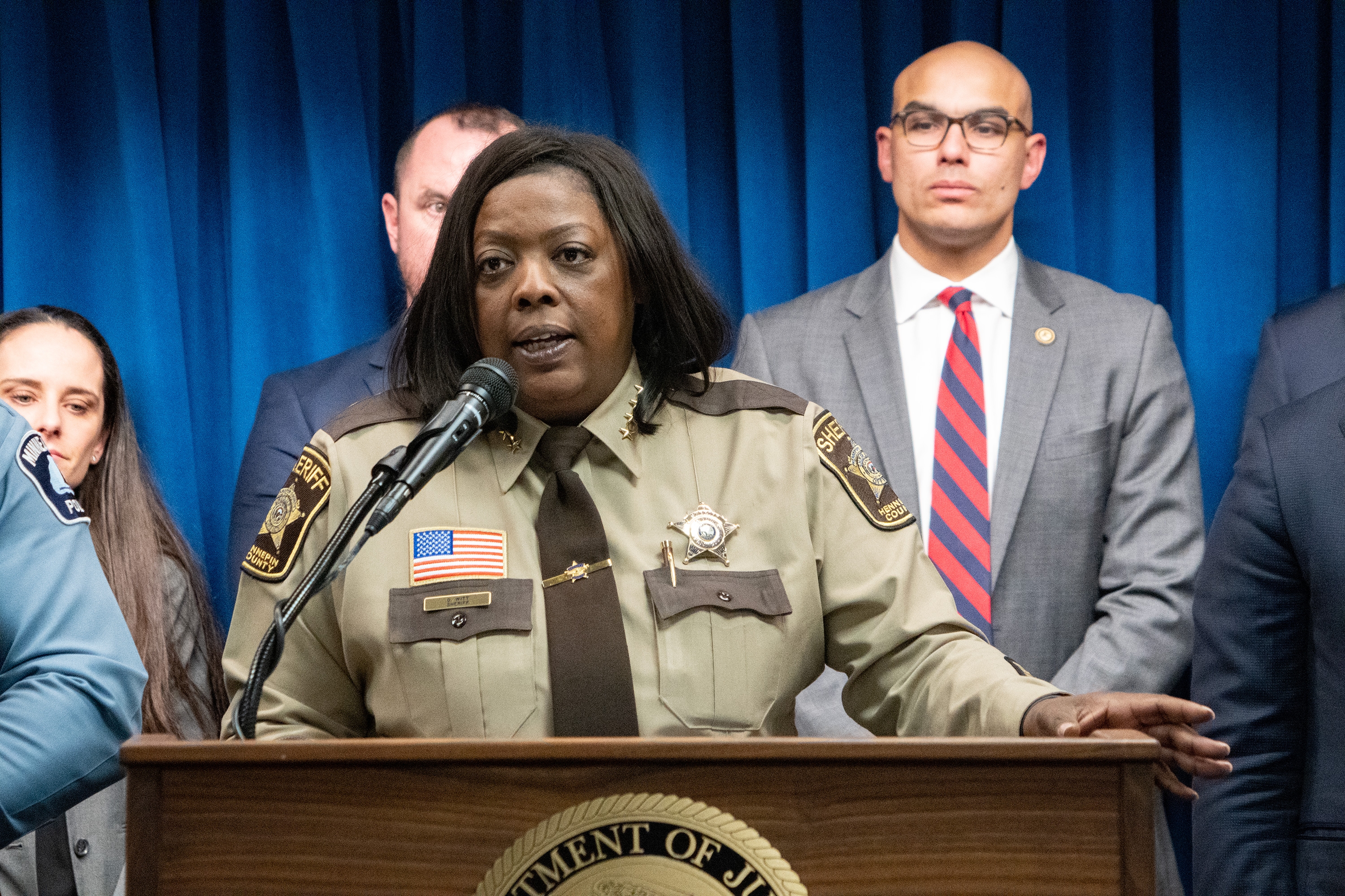 Hennepin County Sheriff Dawanna S. Witt delivers remarks from a podium at the United States Attorney’s Office for the District of Minnesota office in Minneapolis, Minnesota. Other officials stand in a row behind.