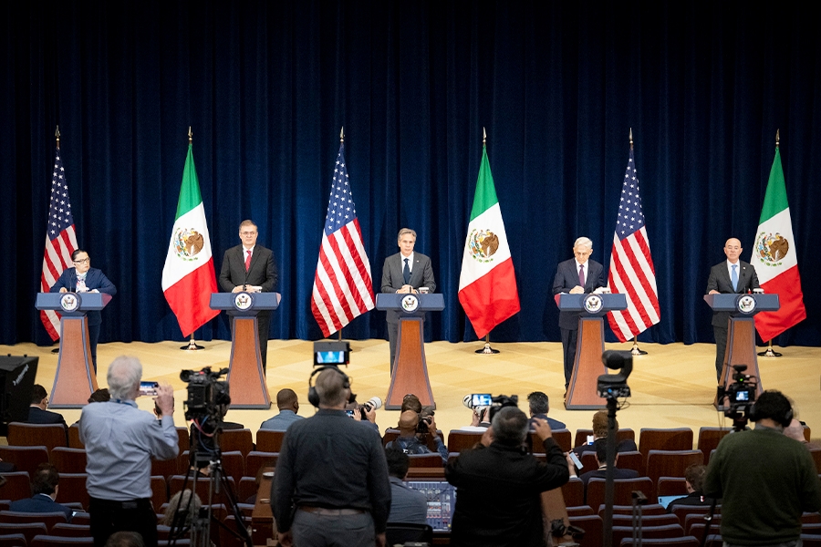 U.S. and Mexico officials stand on a stage with the flags of the United States and Mexico in the background