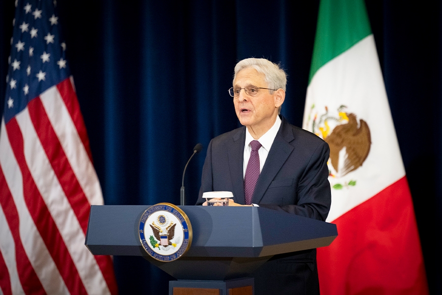 Attorney General Merrick B. Garland speaks at a podium bearing the Department of State seal. The flags of the United States and Mexico are seen in the background