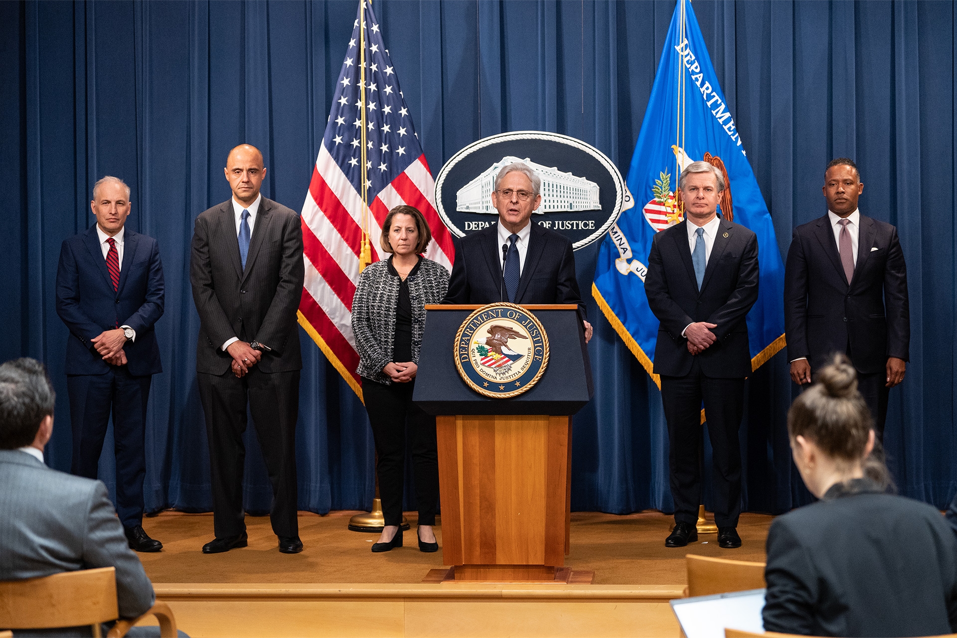 Attorney General Garland delivers remarks from a podium. Behind him stand (from left to right) Assistant Attorney General Olsen, U.S. Attorney Graves, Deputy Attorney General Monaco, FBI Director Wray, and Assistant Attorney General Polite