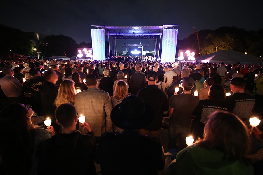 An illuminated stage at the 35th Annual Candlelight Vigil for National Police Week with hundreds of attendees standing before it with lit candles.