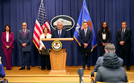 Attorney General Merrick B. Garland delivers remarks from a podium at the Department of Justice. He is joined by Department of Justice and federal government officials.