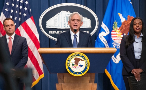 Attorney General Merrick B. Garland delivers remarks from a podium at the Department of Justice. He is joined by Department of Justice and federal government officials.