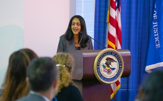 Associate Attorney General Vanita Gupta addresses the crowd from a podium bearing an Office of Justice Programs seal. The American flag and the Department of Justice flag are seen in the background.