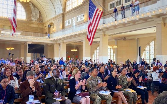 The audience in the Great Hall of Ellis Island in New York applauds in celebration.