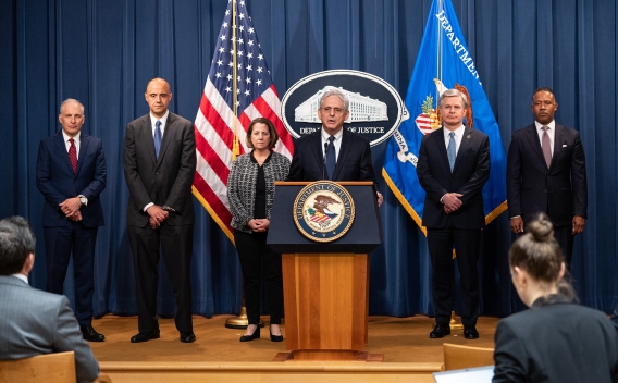 Attorney General Garland delivers remarks from a podium. Behind him stand (from left to right) Assistant Attorney General Olsen, U.S. Attorney Graves, Deputy Attorney General Monaco, FBI Director Wray, and Assistant Attorney General Polite