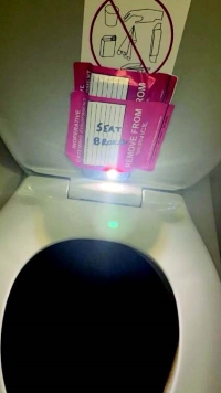 red stickers on the underside lid of aircraft toilet seat, in the open position, that state, “INOPERATIVE CATERING EQUIPMENT” and “REMOVE FROM SERVICE,” and “SEAT BROKEN"