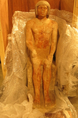 Goldish-brown ancient Egyptian statue sitting against gray bubble wrap 