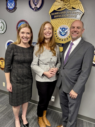 Three people stand for a photo. The person in the middle is holding an award.