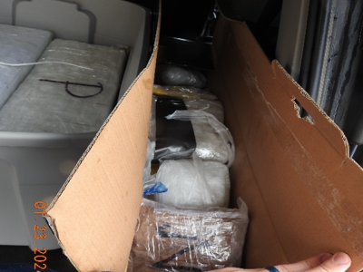 Photograph of packages of methamphetamine wrapped in plastic wrap and other materials. Packages are stacked inside cardboard box.