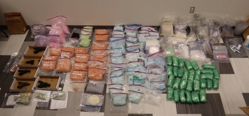 Spread of items seized during takedown: multiple firearms, dozens of plastic bags containing narcotics, cash, other drug trafficking items