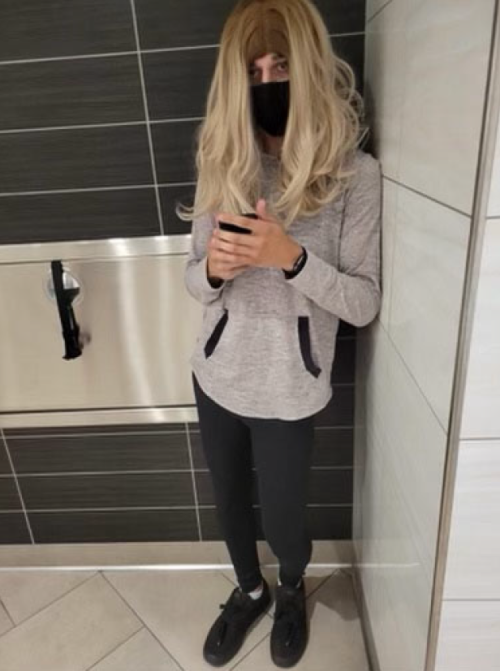 Image of person in blonde wig in bathroom stall wearing face mask
