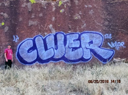 Person standing in front of Cluer and Velor graffiti on rock face.